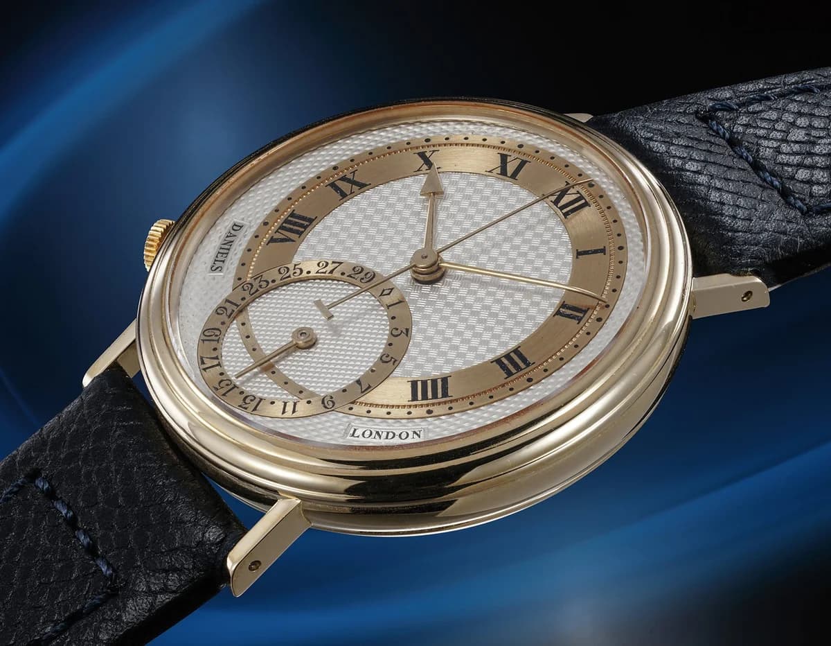 George Daniels Millennium in 18K yellow gold. The engine-turned silver dial with gold chapter ring, Roman numerals, and date subdial at 6 o'clock.