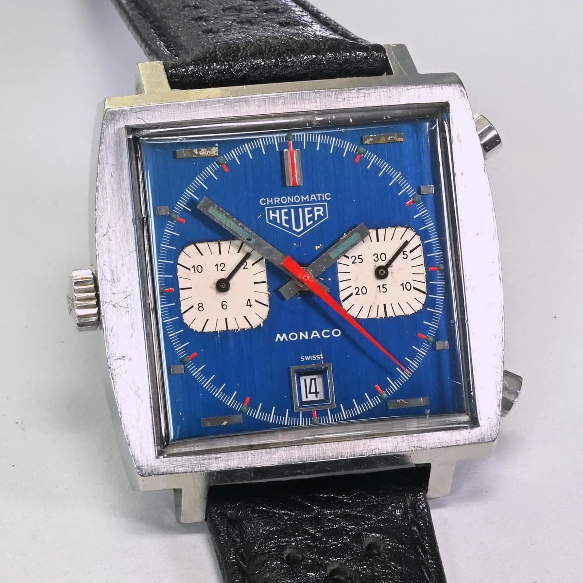 Heuer Monaco 1133B Chronomatic with the iconic metallic blue dial, white subsidiary registers, and left-side crown at 9 o'clock.