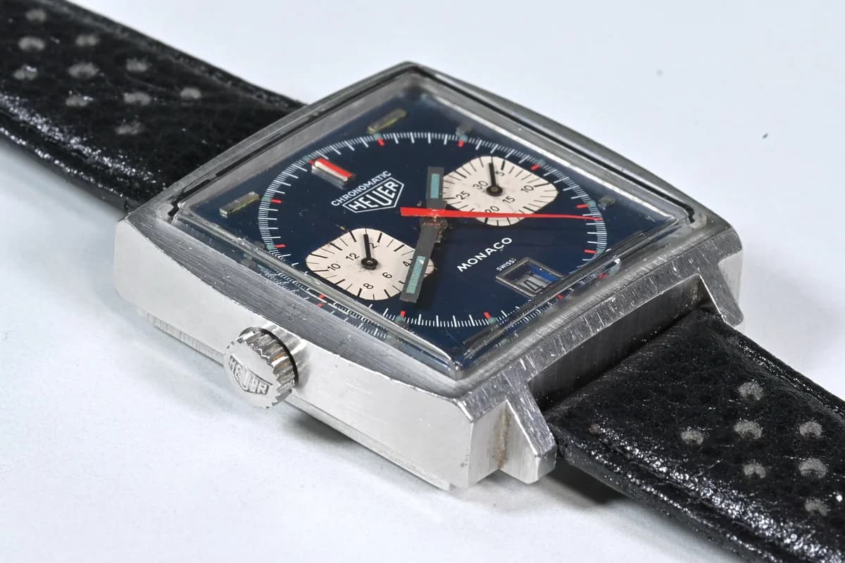 Three-quarter view showing the Monaco's sharp square geometry and the contrast between brushed steel case and blue dial.