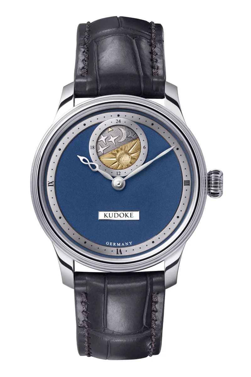 Blued infinity-symbol hour hand and Kudoke nameplate against the frosted dial surface